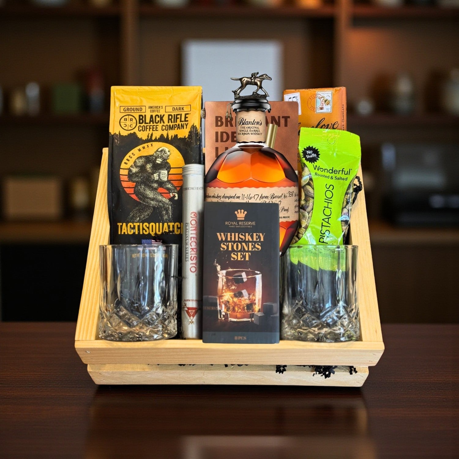 Blanton’s Original Single Barrel Top Shelf Gift Crate featuring engravable bourbon bottle and glasses, coffee, chocolate, pistachios, cigar, and whiskey stones on bar – Top Bourbon lifestyle photo