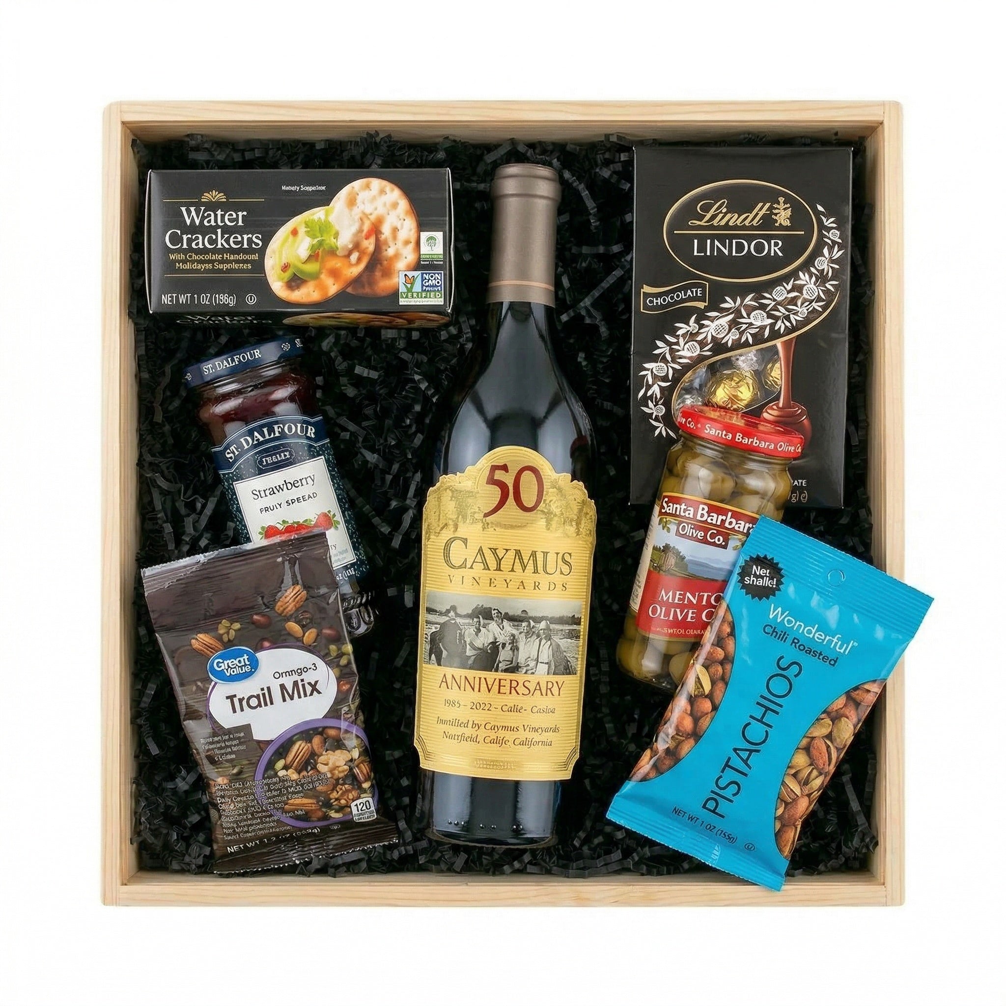 Caymus Vineyards Cabernet Sauvignon anniversary wine gift set with Lindt Lindor chocolates, pistachios, olives, strawberry fruit spread, crackers and trail mix arranged in wooden gift crate