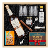 Basil Hayden's Old-Fashioned cocktail gift crate with Basil Hayden's Kentucky Straight Bourbon Whiskey with copper band and cork cap, crystal-cut old fashioned glasses, Angostura bitters, premium muddler, bar spoon, jigger, Peninsula cocktail cherries, La Perruche sugar cubes, and Royal Reserve whiskey stones set all nestled in black zigzag crinkle paper inside wooden crate on white background