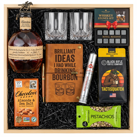 Blanton's Original Single Barrel Bourbon Top Shelf gift crate with bronze horse stopper, crystal-cut old fashioned glasses, Royal Reserve whiskey stones set with tray, faux-leather bourbon journal and pen set, Montecristo Platinum cigar tube, Black Rifle Coffee Tactisquatch blend, Chocolove Almonds & Sea Salt dark chocolate bar, and Wonderful Pistachios in black crinkle paper on white background