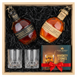 Blanton's Takara Black Edition and Blanton's Takara Red Edition dual-bottle gift crate with bronze horse stoppers and Japanese labels, crystal-cut old fashioned glasses, and Royal Reserve whiskey stones gift box with red ribbon all nestled in black zigzag crinkle paper inside wooden crate on white background