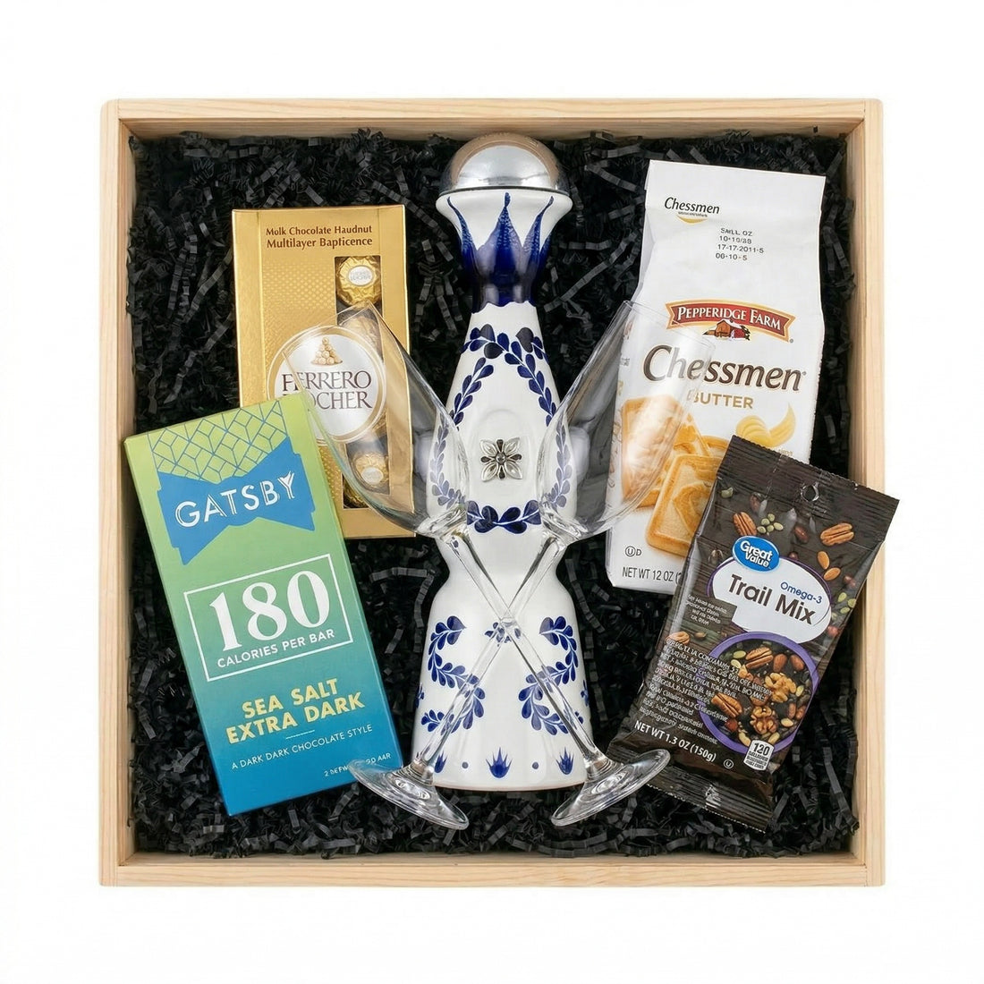 Clase Azul Reposado tequila gift crate with Ferrero Rocher chocolates, Gatsby dark chocolate, Chessmen cookies, trail mix and tequila flutes displayed in wooden gift crate by fireplace