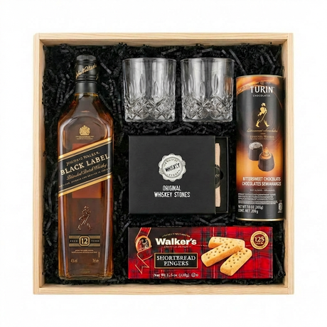 Johnnie Walker Black Label 12 Year Scotch Gift Crate featuring a 750ml bottle, two crystal cut whiskey glasses, Original Whiskey Stones set, Walker's Shortbread Fingers, and Turin Johnnie Walker Bittersweet Chocolates tube, arranged in a light wooden gift box with black crinkle paper