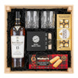 The Macallan 15 Year Old Double Cask Single Malt Scotch gift crate with crystal-cut old fashioned glasses, premium whiskey stones gift set, Ferrero Rocher chocolates, and Walker's shortbread fingers in black crinkle paper on white background